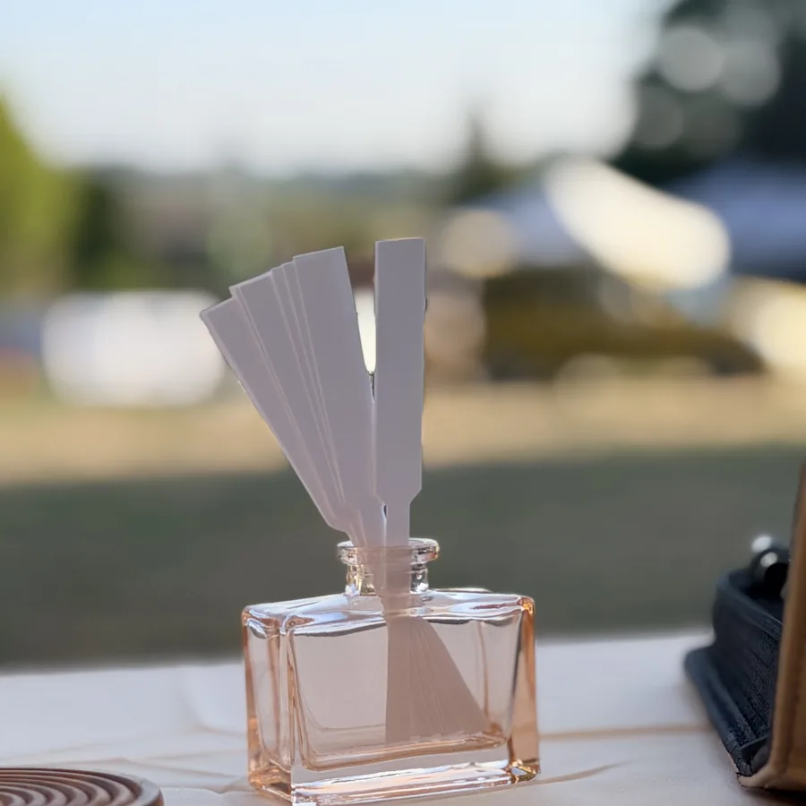 Un flacon en verre rosé garni de touches à sentir, sur la table d'un bar à parfums en plein air
